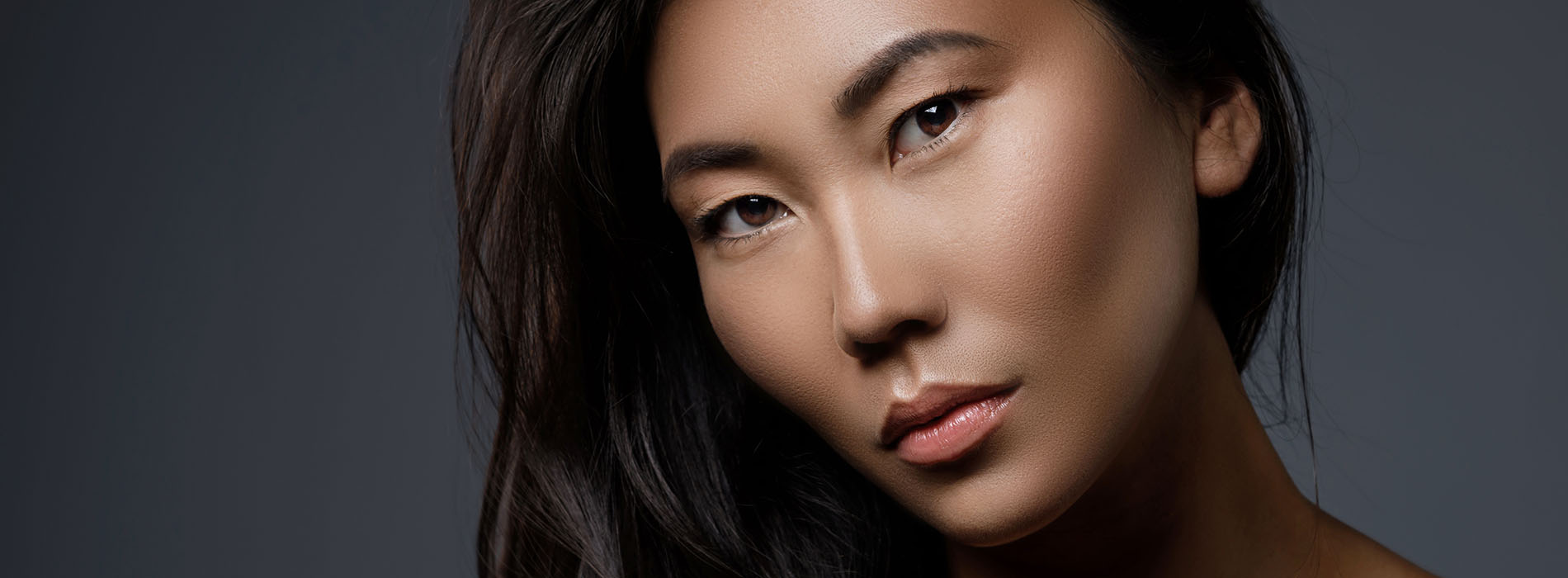 The image features a woman with long hair against a dark background, showcasing her profile while looking directly at the camera.