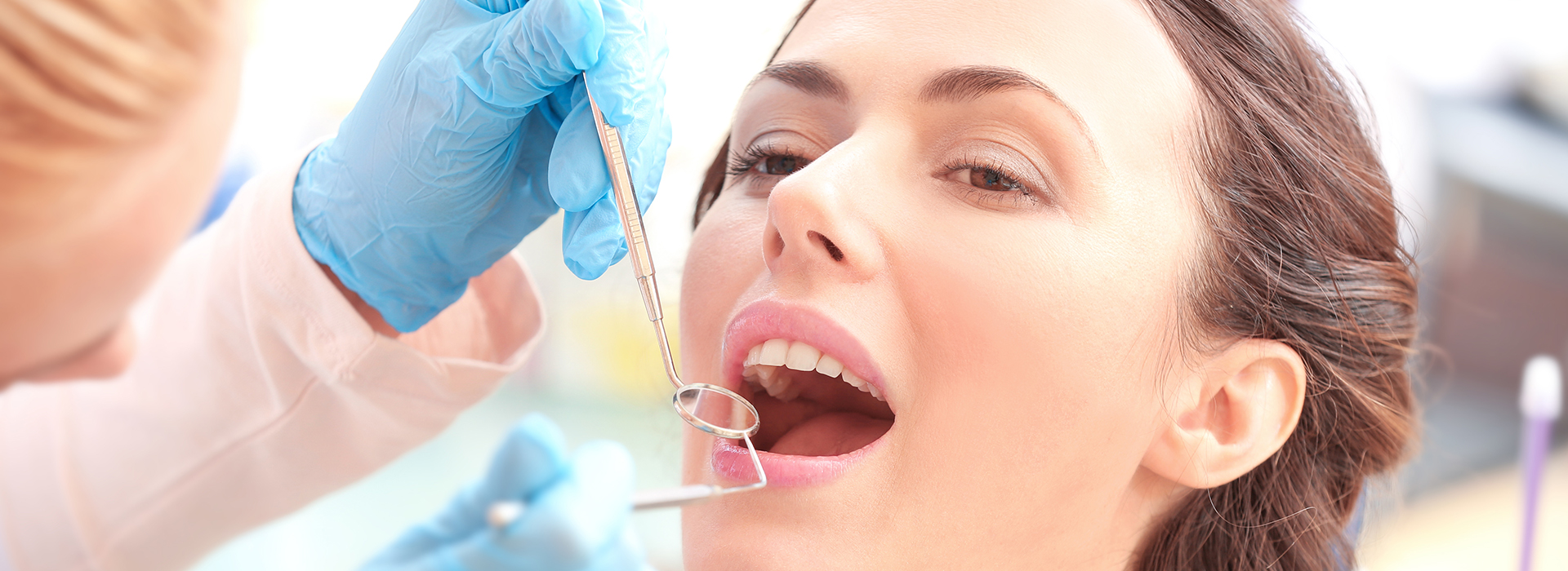 Woman receiving dental treatment with dental tools visible.