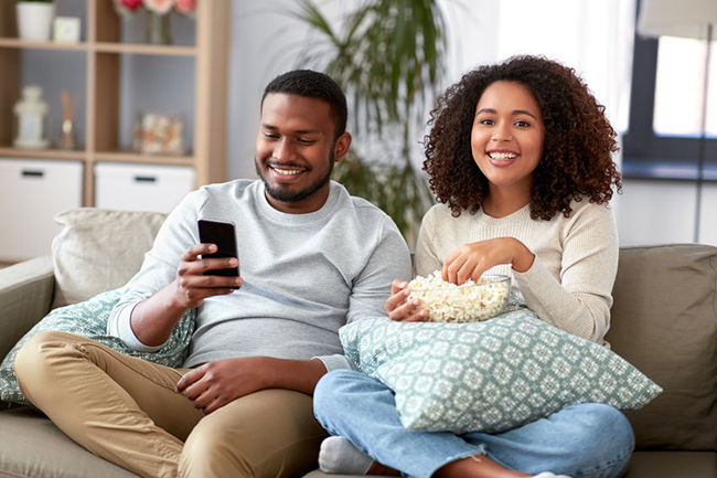 A couple sitting on a couch, sharing a moment with popcorn while watching TV.